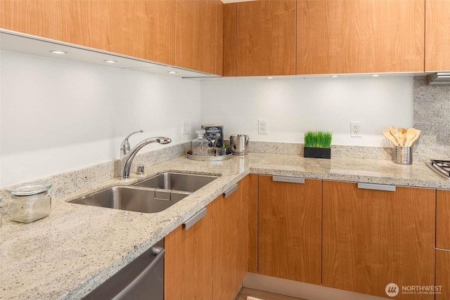 kitchen with brown cabinetry, modern cabinets, a sink, and light stone countertops