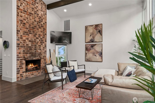 living room with visible vents, lofted ceiling with beams, wood finished floors, a fireplace, and baseboards