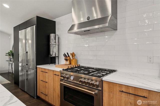 kitchen featuring tasteful backsplash, dark wood-type flooring, wall chimney range hood, high quality appliances, and light stone counters