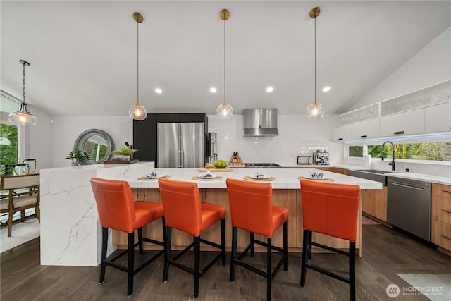 kitchen featuring vaulted ceiling, wall chimney range hood, modern cabinets, and appliances with stainless steel finishes