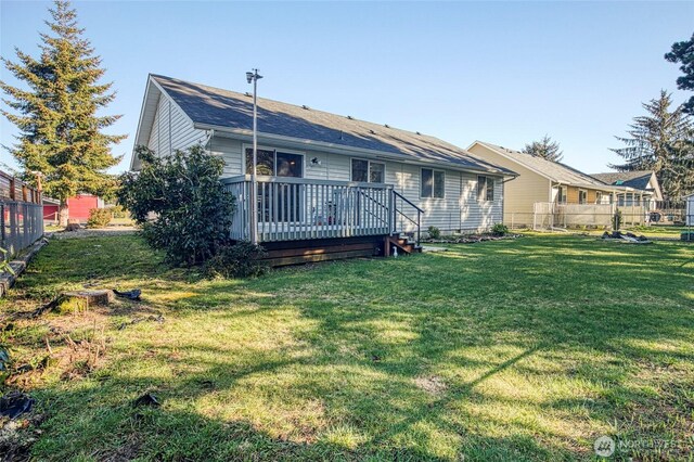 rear view of house featuring a deck, a lawn, and fence