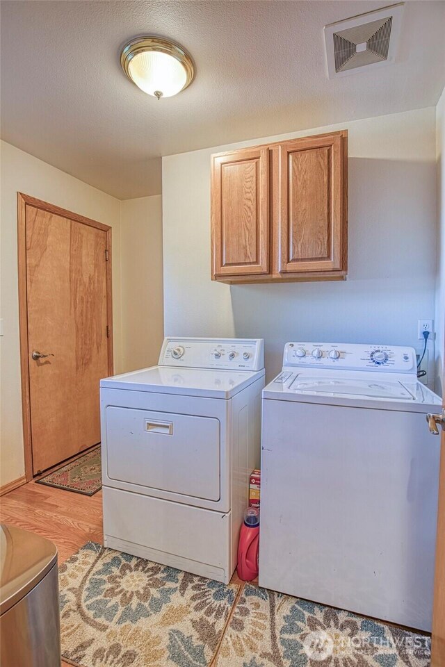 laundry room featuring visible vents, cabinet space, washing machine and dryer, a textured ceiling, and light wood-type flooring