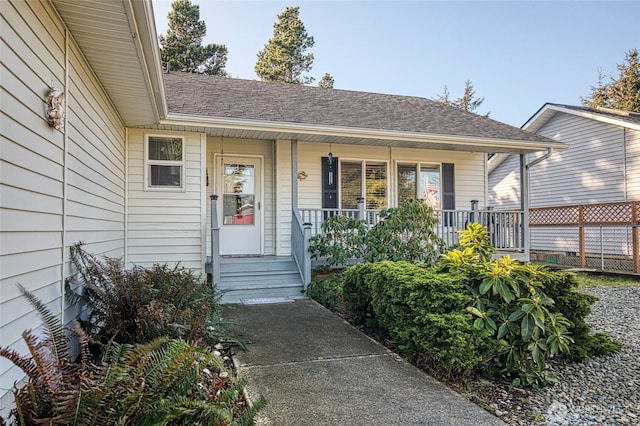 entrance to property with covered porch and a shingled roof