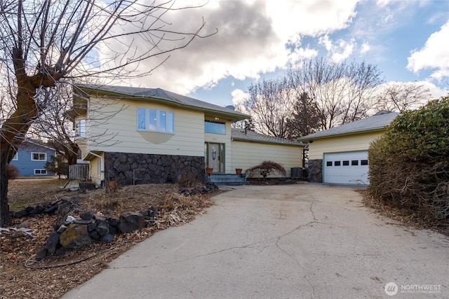 view of front of house with an outbuilding, central air condition unit, an attached garage, stone siding, and driveway