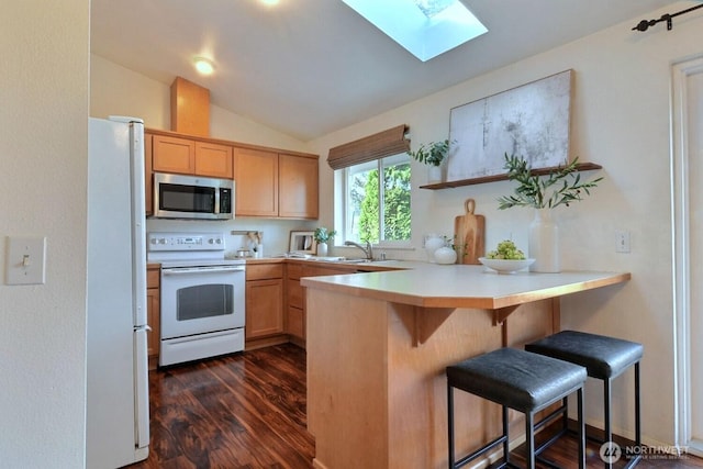 kitchen featuring dark wood finished floors, light countertops, lofted ceiling with skylight, white appliances, and a peninsula