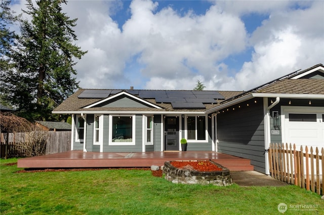 rear view of property with a deck, an attached garage, solar panels, fence, and a lawn