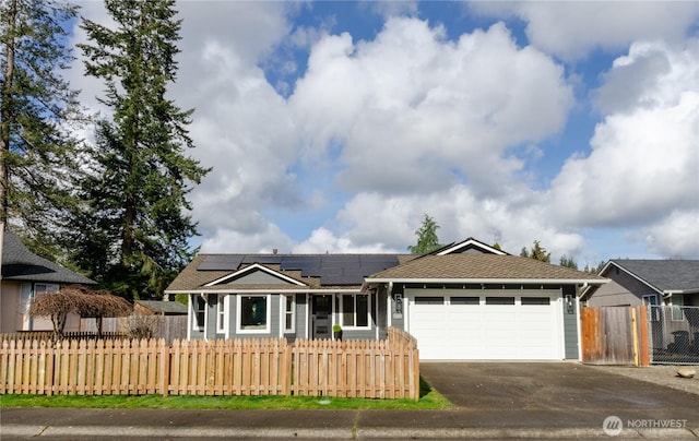 ranch-style house featuring a garage, aphalt driveway, a fenced front yard, and roof mounted solar panels