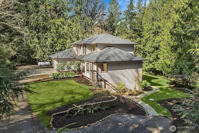 view of front facade with driveway, roof with shingles, and a front yard