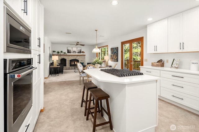 kitchen featuring a breakfast bar area, stainless steel appliances, a brick fireplace, white cabinetry, and ceiling fan