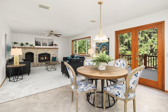 dining space featuring french doors, light colored carpet, visible vents, a brick fireplace, and ceiling fan