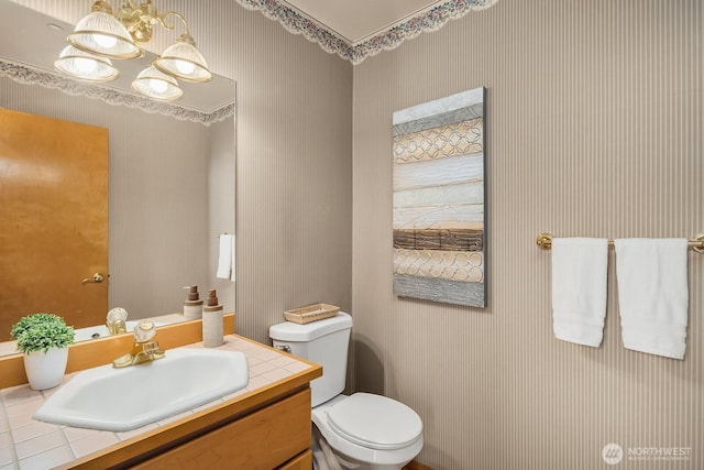 bathroom with wallpapered walls, vanity, toilet, and an inviting chandelier