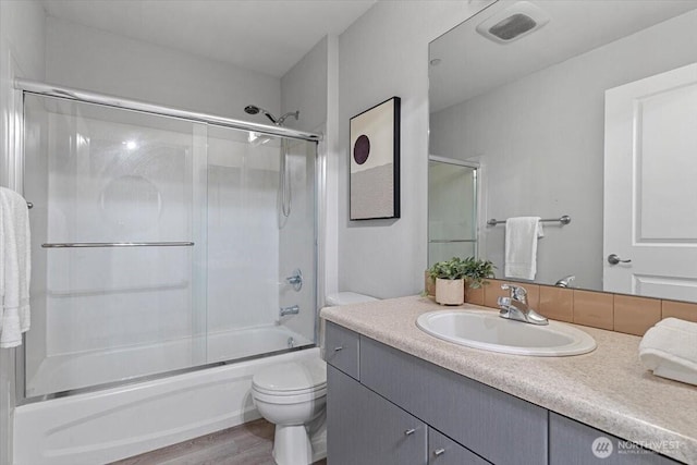 full bath featuring visible vents, toilet, wood finished floors, combined bath / shower with glass door, and vanity