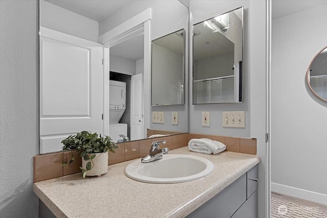 bathroom featuring vanity, stacked washer / drying machine, and baseboards