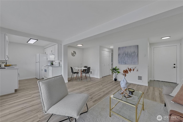 living room with light wood finished floors, visible vents, and baseboards