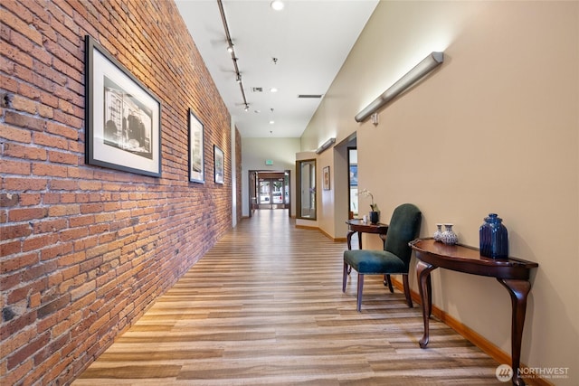 hall with brick wall, visible vents, baseboards, light wood-type flooring, and rail lighting