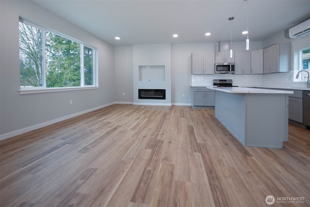 kitchen with a wall unit AC, gray cabinetry, stainless steel appliances, light countertops, and backsplash