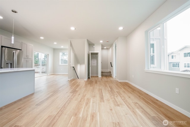 unfurnished living room with recessed lighting, baseboards, light wood finished floors, and stairs