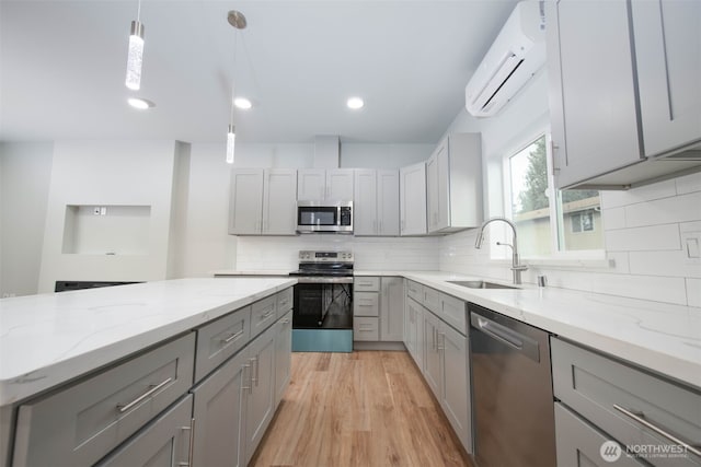 kitchen featuring appliances with stainless steel finishes, an AC wall unit, gray cabinetry, light wood-type flooring, and a sink