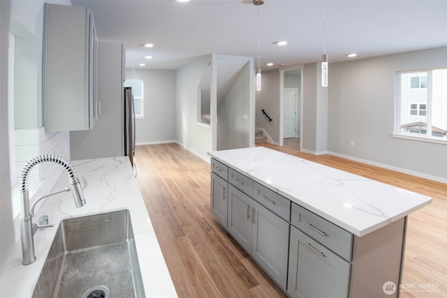 kitchen featuring light stone counters, pendant lighting, gray cabinets, a sink, and light wood-type flooring