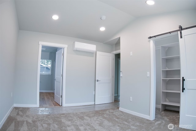 unfurnished bedroom featuring carpet floors, an AC wall unit, a spacious closet, and a barn door