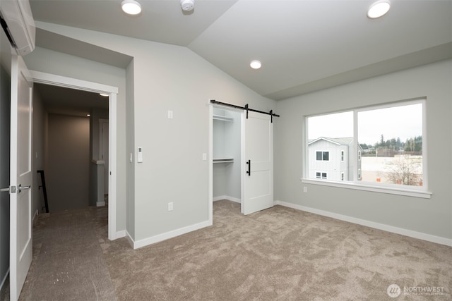 unfurnished bedroom featuring a walk in closet, carpet, lofted ceiling, a barn door, and baseboards