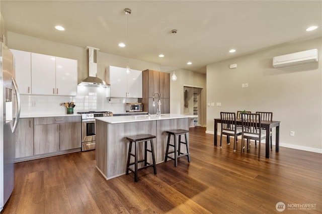 kitchen featuring an AC wall unit, appliances with stainless steel finishes, wall chimney range hood, modern cabinets, and a kitchen bar