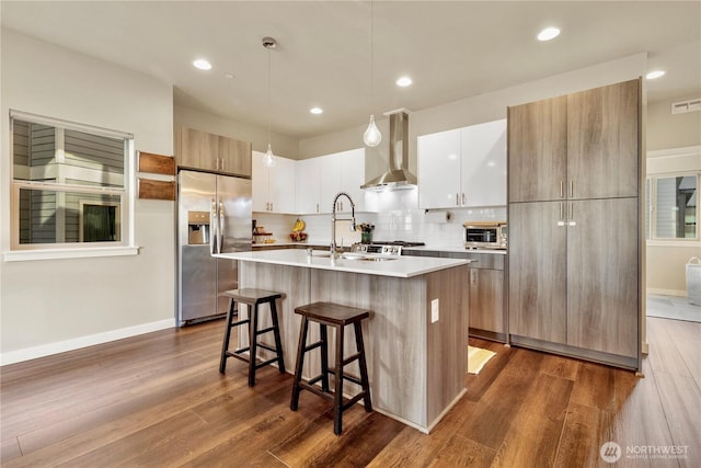 kitchen featuring wall chimney exhaust hood, a sink, stainless steel fridge with ice dispenser, and modern cabinets