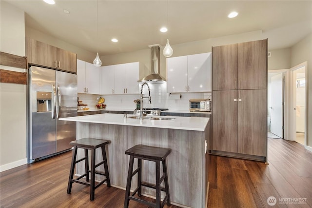 kitchen with dark wood-style flooring, stainless steel refrigerator with ice dispenser, backsplash, wall chimney exhaust hood, and modern cabinets