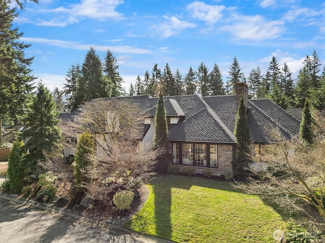 tudor home with a shingled roof, brick siding, a chimney, and a front lawn