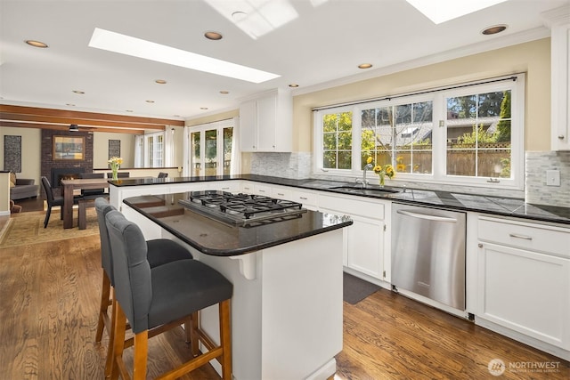 kitchen featuring dark countertops, stainless steel appliances, a skylight, and a sink