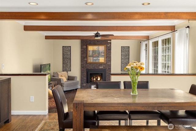 dining area with baseboards, ornamental molding, wood finished floors, a brick fireplace, and beam ceiling