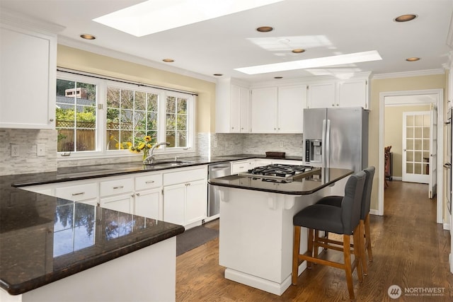 kitchen featuring stainless steel appliances, a skylight, white cabinets, and ornamental molding