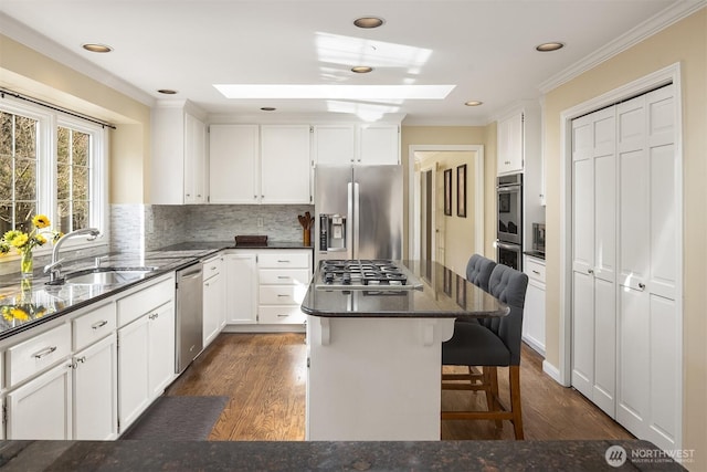 kitchen featuring a skylight, a breakfast bar, crown molding, stainless steel appliances, and a sink