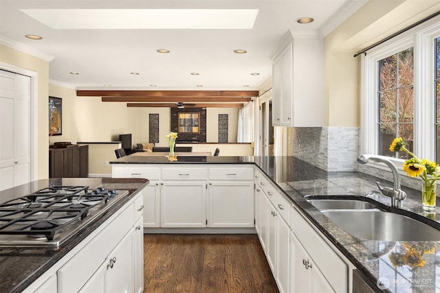 kitchen with dark wood-style floors, a skylight, stainless steel gas stovetop, a sink, and a peninsula