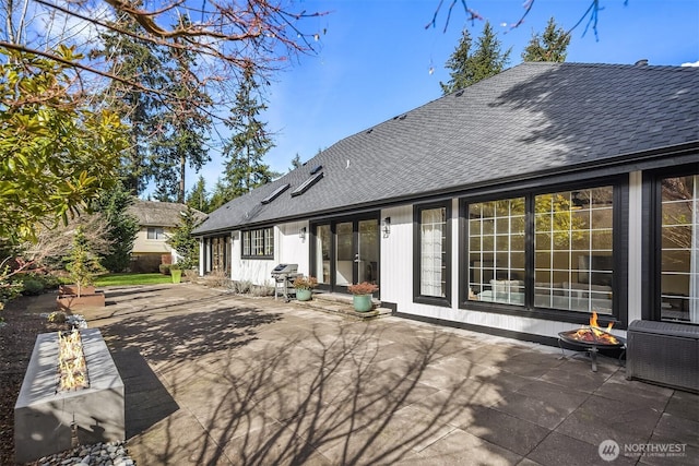 rear view of property with a shingled roof, an outdoor fire pit, and a patio