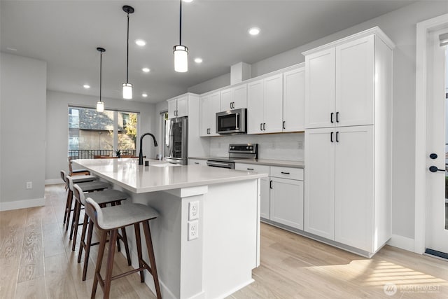 kitchen featuring light wood-type flooring, an island with sink, a sink, white cabinetry, and stainless steel appliances