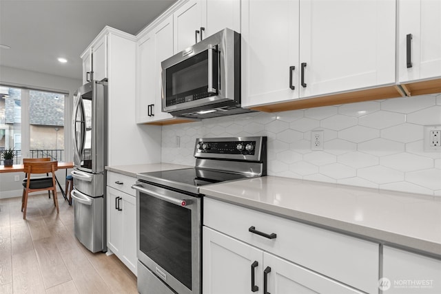 kitchen with tasteful backsplash, light wood-type flooring, light countertops, appliances with stainless steel finishes, and white cabinets