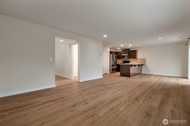 unfurnished living room featuring light wood-style flooring, recessed lighting, baseboards, and a sink