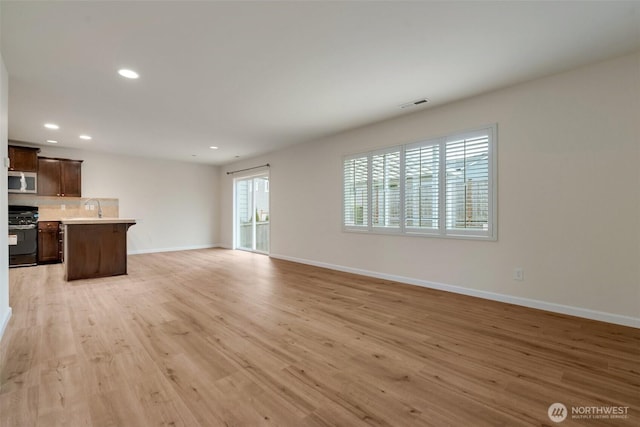 unfurnished living room featuring visible vents, a sink, recessed lighting, light wood-style floors, and baseboards