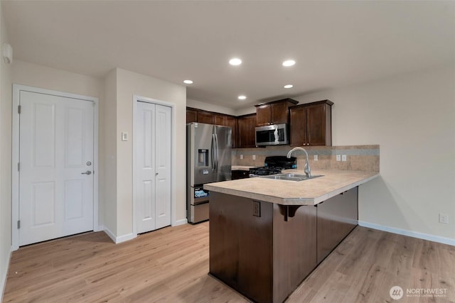 kitchen featuring a peninsula, a sink, stainless steel appliances, light countertops, and dark brown cabinetry