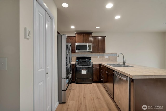 kitchen with light wood-style flooring, a sink, stainless steel appliances, light countertops, and tasteful backsplash