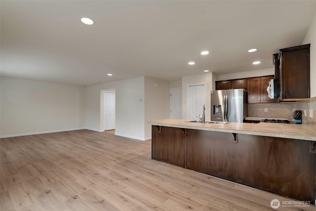 kitchen featuring a peninsula, stainless steel fridge with ice dispenser, a sink, dark brown cabinetry, and a kitchen breakfast bar