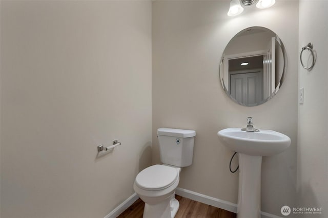 half bath with toilet, wood finished floors, baseboards, and a sink