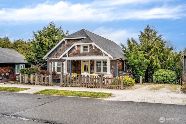 view of front of house with driveway, a fenced front yard, a porch, and a shingled roof