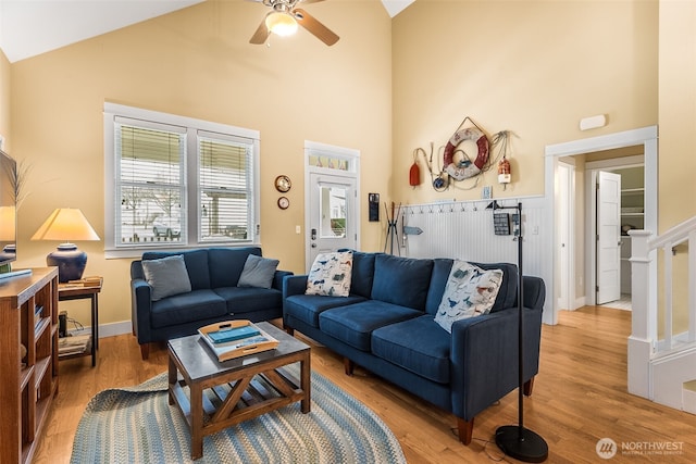 living room featuring light wood finished floors, high vaulted ceiling, a ceiling fan, and a wainscoted wall