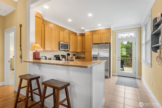 kitchen with light tile patterned floors, stone countertops, appliances with stainless steel finishes, a breakfast bar, and a peninsula