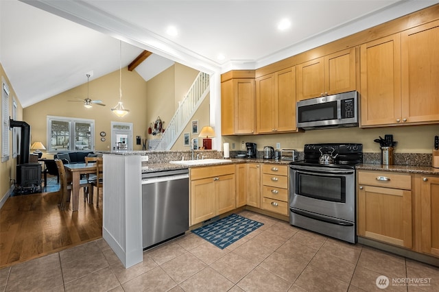 kitchen with light tile patterned floors, stainless steel appliances, a peninsula, dark stone counters, and beamed ceiling