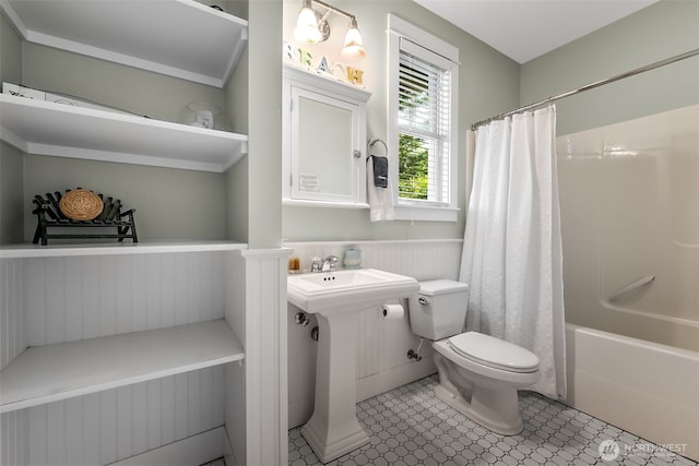 bathroom with a wainscoted wall, toilet, and shower / tub combo with curtain