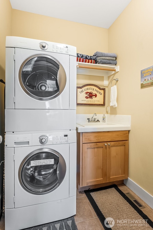 washroom with baseboards, visible vents, stacked washing maching and dryer, a sink, and light tile patterned flooring