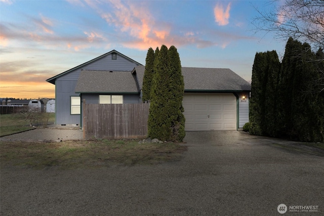 front of property at dusk with an attached garage, fence, driveway, and roof with shingles